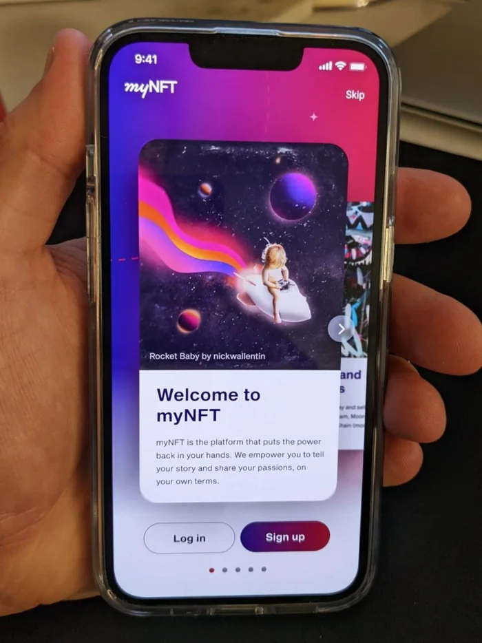 A hand holding a phone showing the myNFT app’s welcome screen, with a featured work titled “Rocket Baby by nickwallentin” and the line “myNFT is the platform that puts the power back in your hands.”